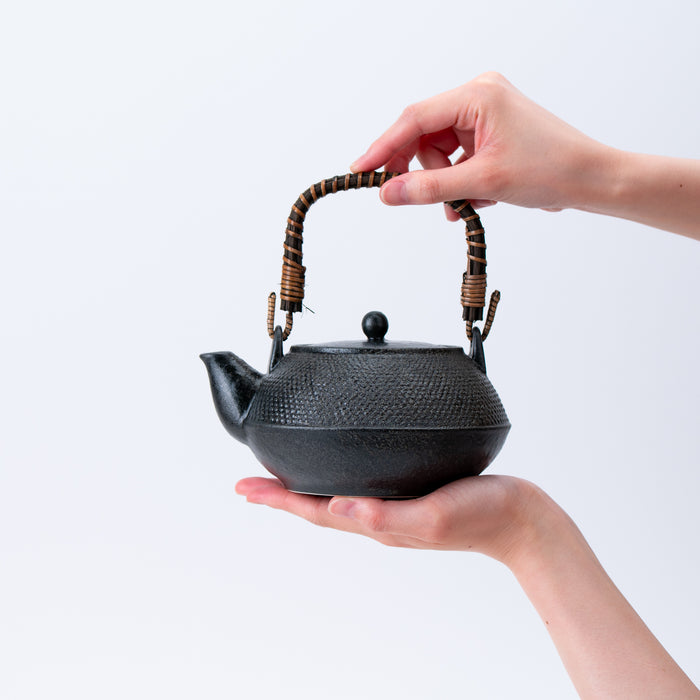 Nambu-style Black Teapot with a hammered iron texture and rattan-wrapped handle, perfect for a traditional Japanese tea ritual.